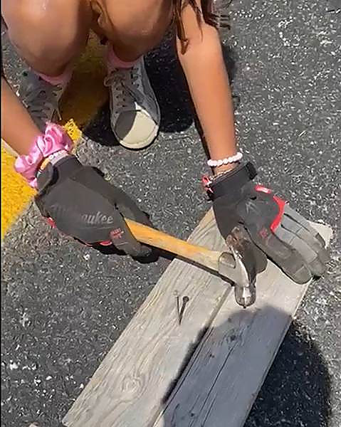 A camper in work gloves hammering a nail into a board during a Hexagon camp week