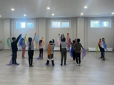 Kids in a circle raising colourful movement scarves during an indoor movement block